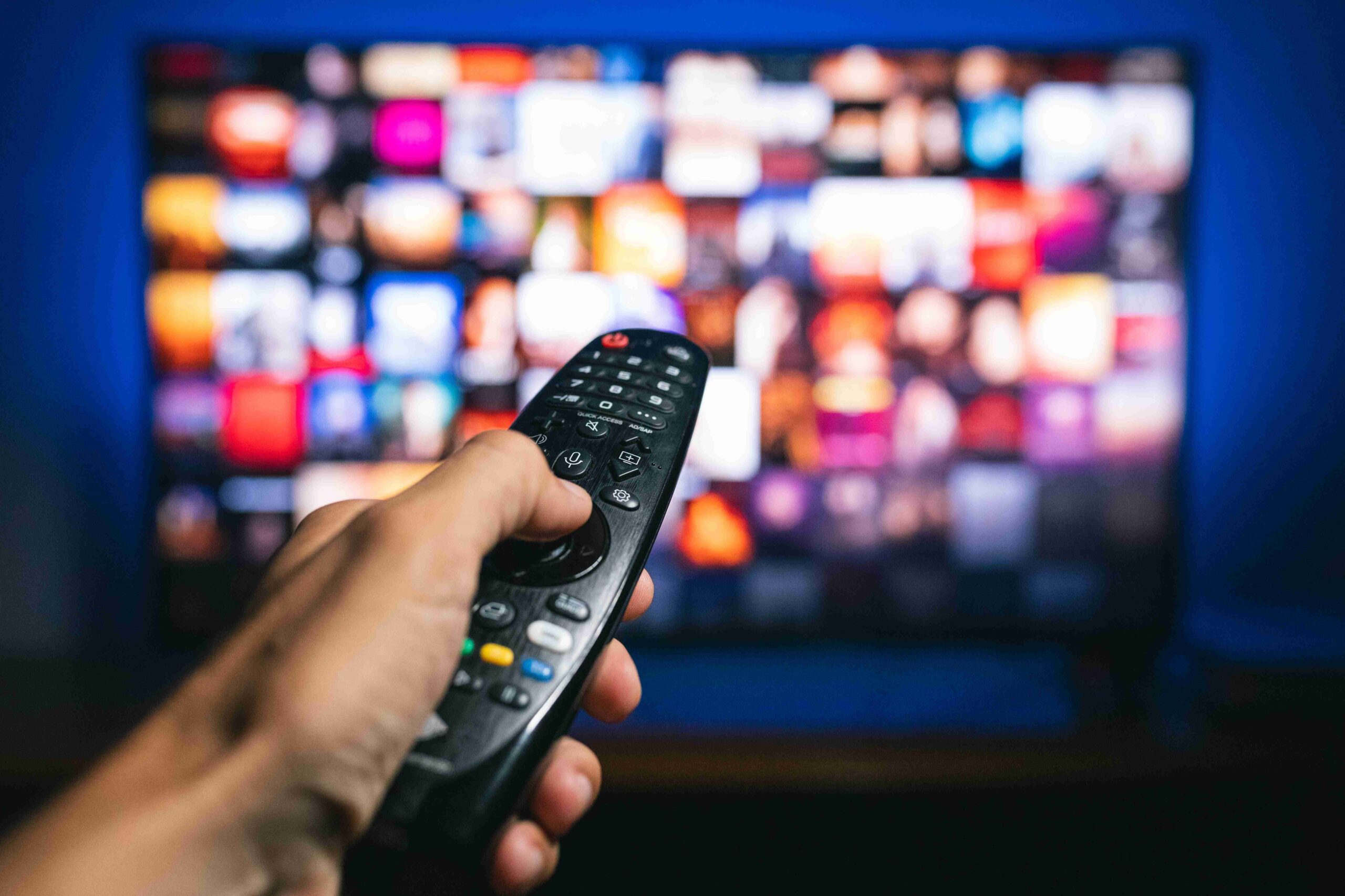Hand holding a remote control in front of a television